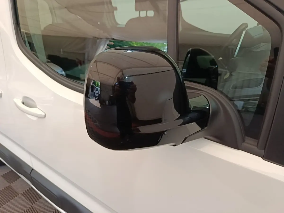 Rétroviseur noir en gros plan sur côté gauche d'un Citroën Berlingo blanc, vue latérale partielle.