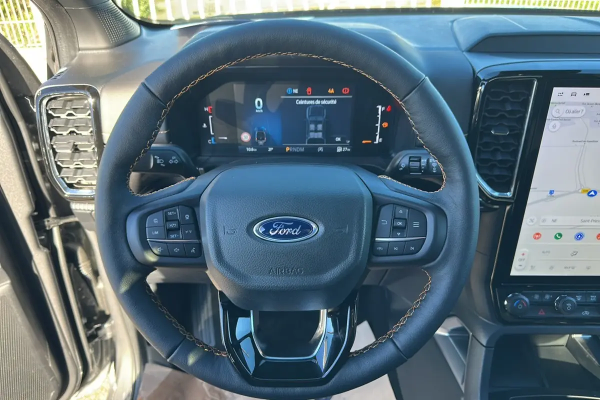 Vue rapprochée du volant cuir noir avec coutures marron et tableau de bord numérique du Ford Ranger gris carbone 2025.