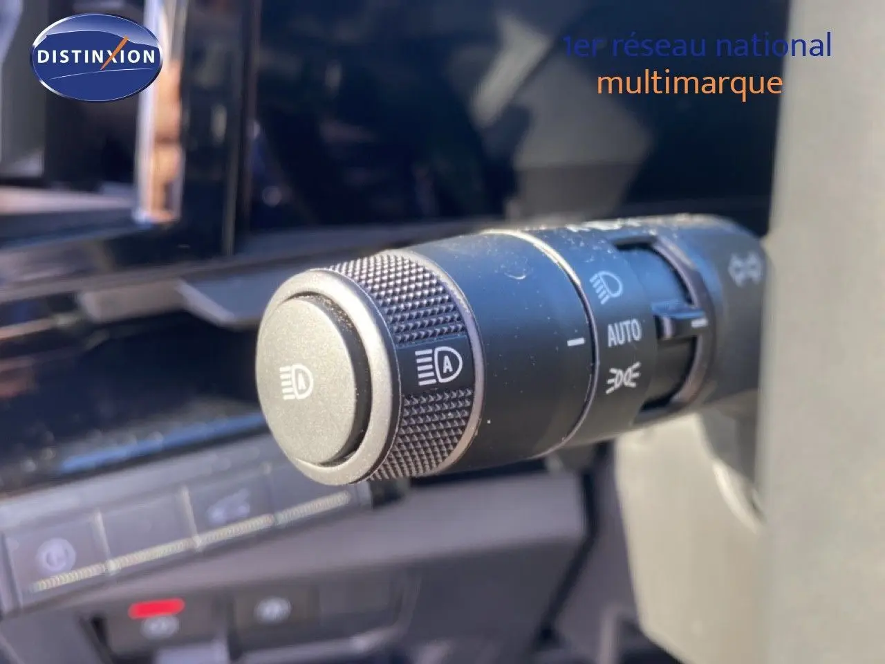 Gros plan sur la commande des feux avec réglage automatique dans l'habitacle du Renault Austral blanc nacré 2024.