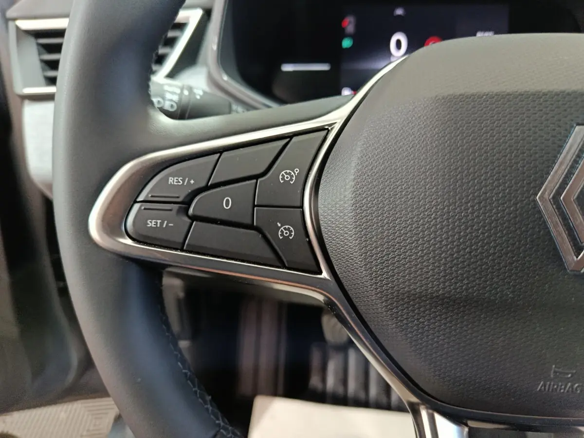 Gros plan sur le volant cuir noir de la Renault Clio 2025 avec commandes de régulateur de vitesse à gauche.