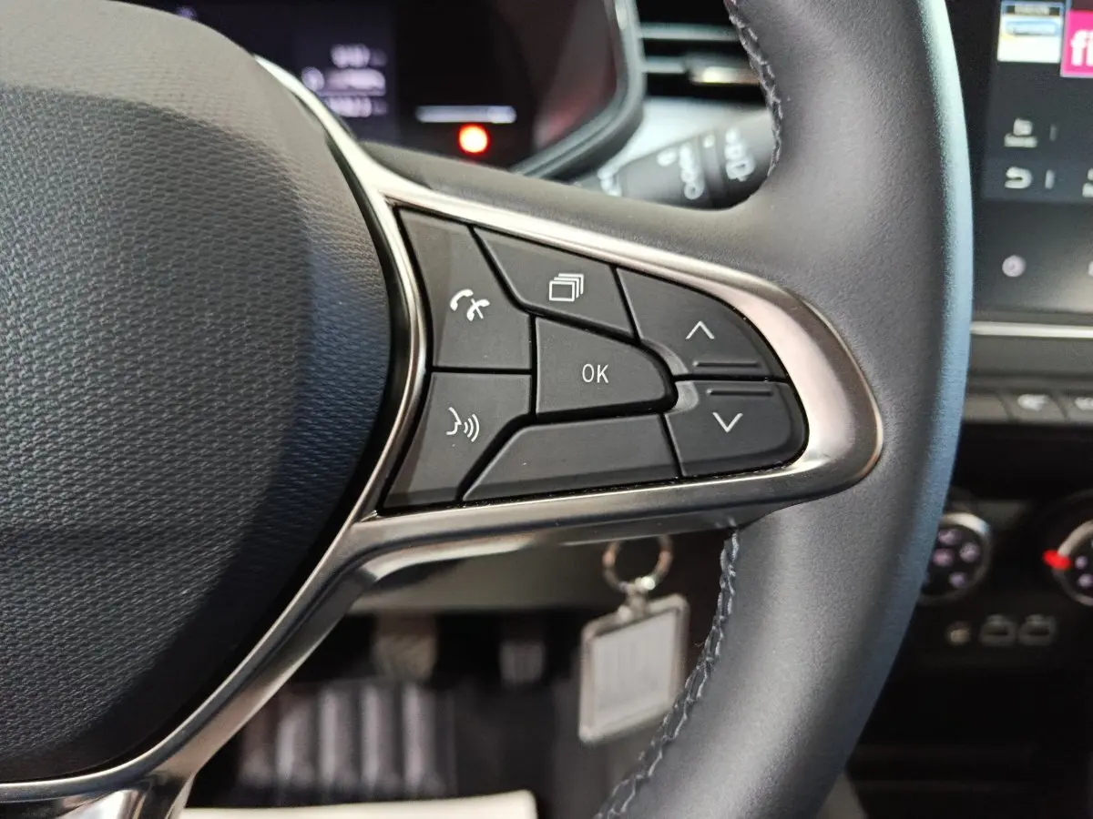 Gros plan sur le volant cuir synthétique de la Renault Clio gris clair, avec commandes multifonctions visibles à droite.