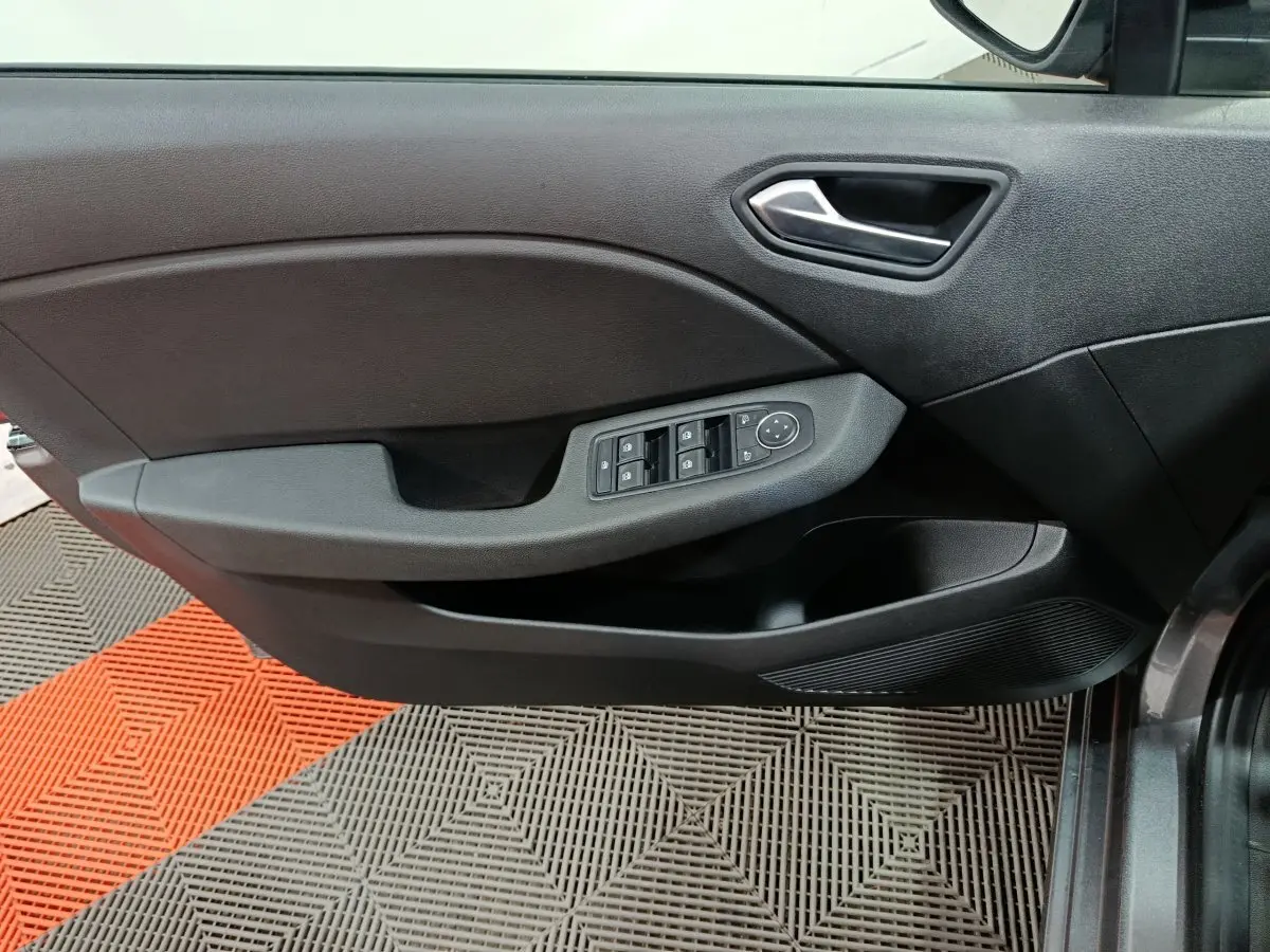 Vue intérieure du panneau de porte côté gauche de la Renault Clio gris clair, avec commandes électriques des vitres et poignée argentée.