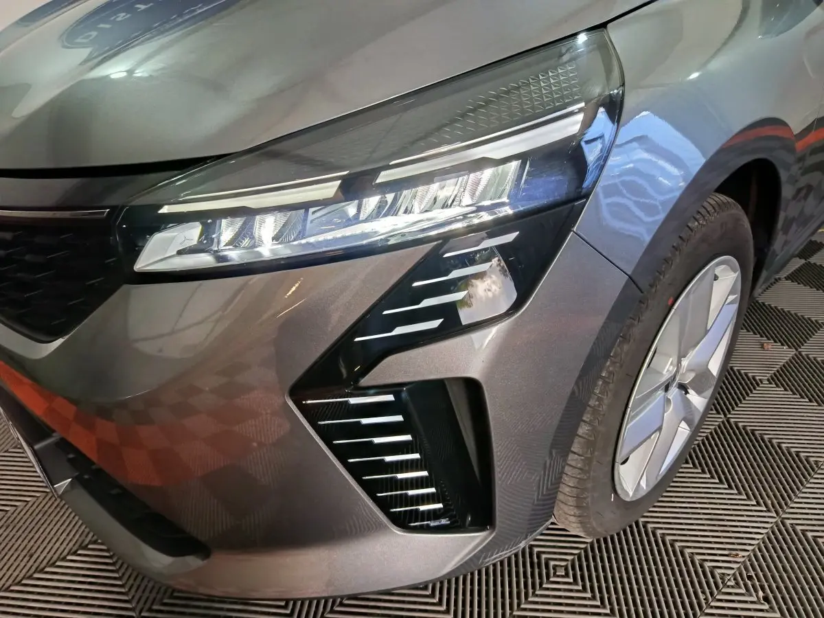 Gros plan sur l'avant droit gris clair de la Renault Clio 2025, mettant en valeur le phare LED et la jante moderne.