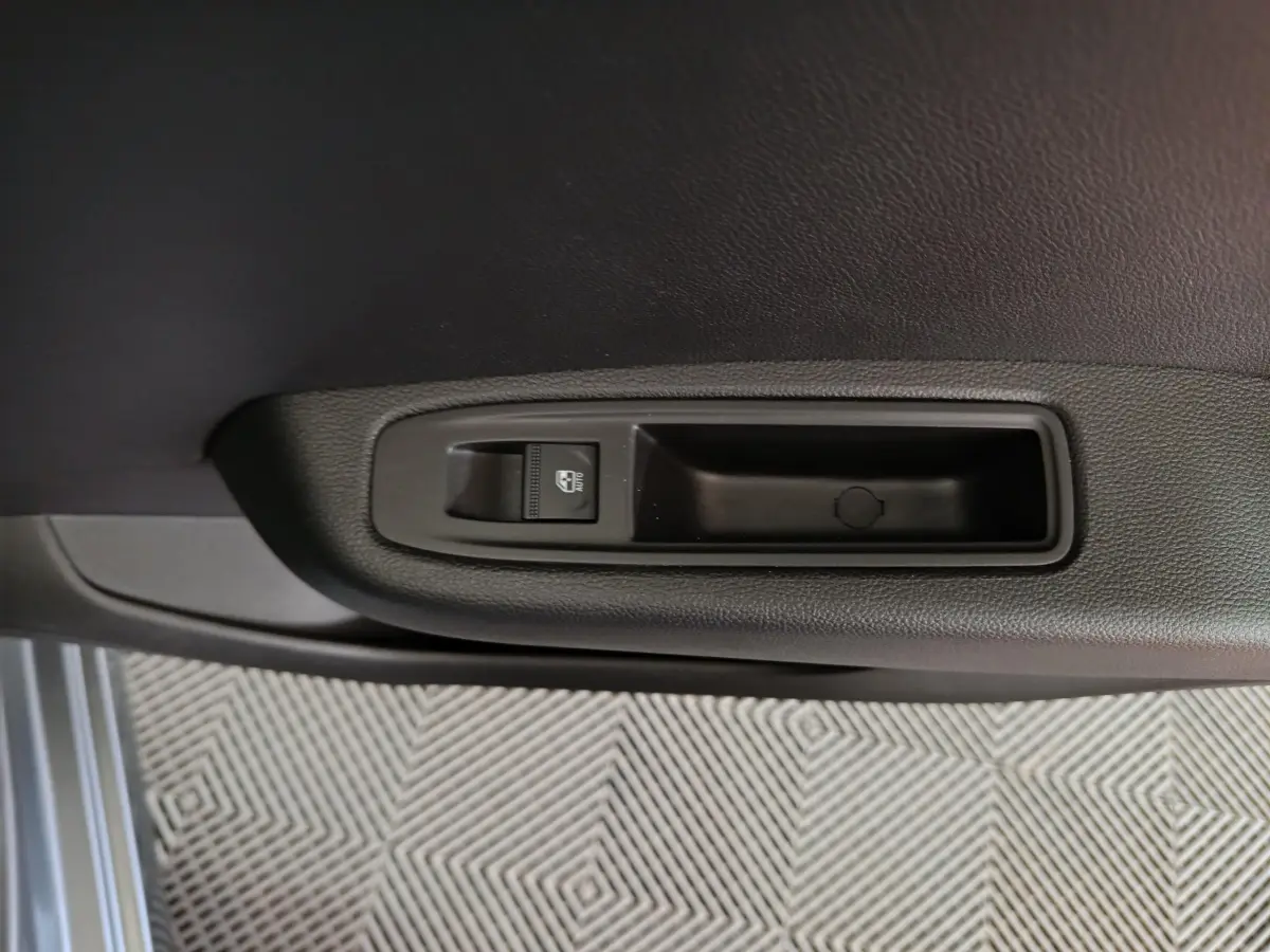 Gros plan sur la commande de lève-vitre électrique côté porte intérieure d’une Renault Clio gris clair.