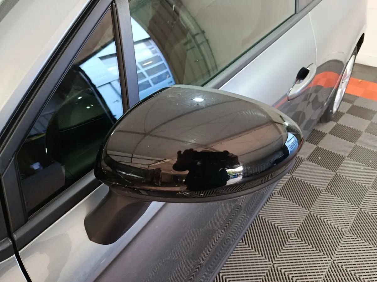 Rétroviseur noir brillant côté gauche d'une Renault Clio gris clair vue en léger angle depuis l'avant.