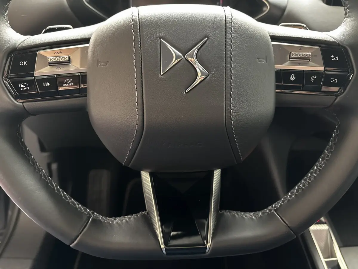 Gros plan sur le volant cuir noir du DS3 2024 avec commandes multifonctions et logo DS central argenté.