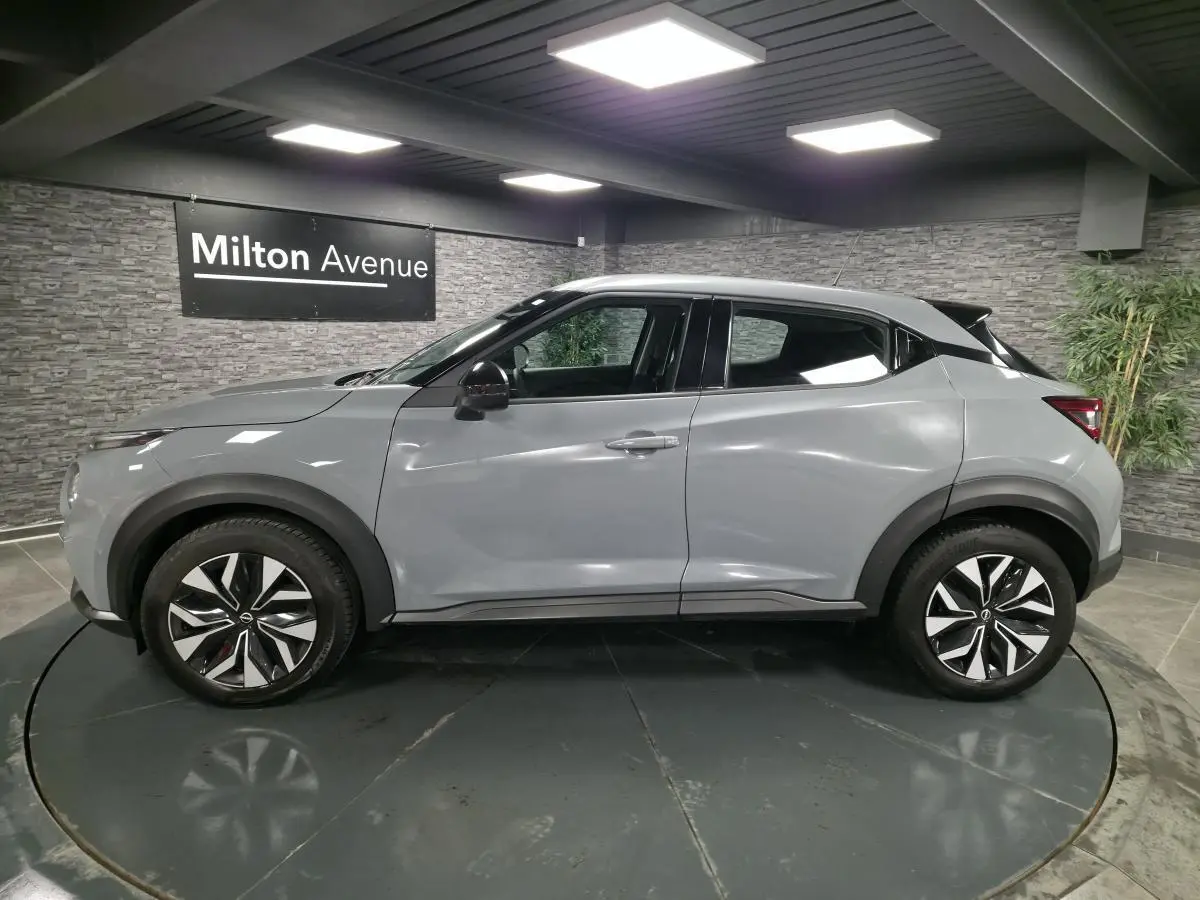 Vue de profil côté gauche d'un Nissan Juke gris métallisé 2023 avec jantes bi-ton et rétroviseurs noirs.