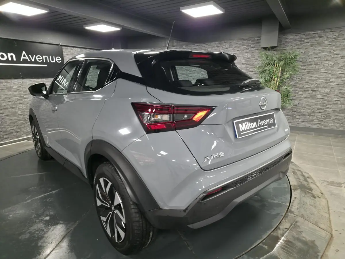 Vue 3/4 arrière droite d'un Nissan Juke gris métallisé 2023 avec jantes bi-ton et toit noir dans un showroom.