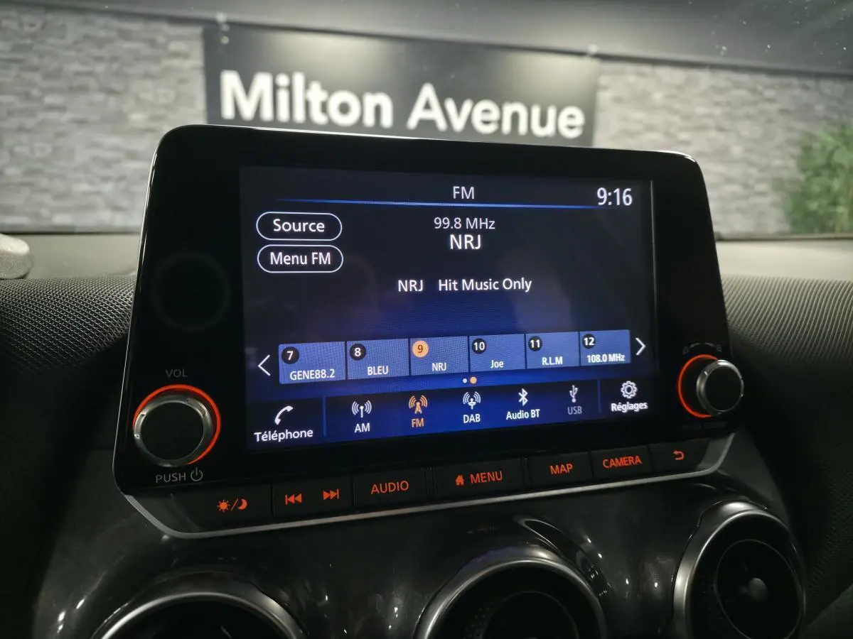 Écran tactile central du tableau de bord du Nissan Juke 2023 affichant la radio FM NRJ, avec commandes audio et climatisation visibles.