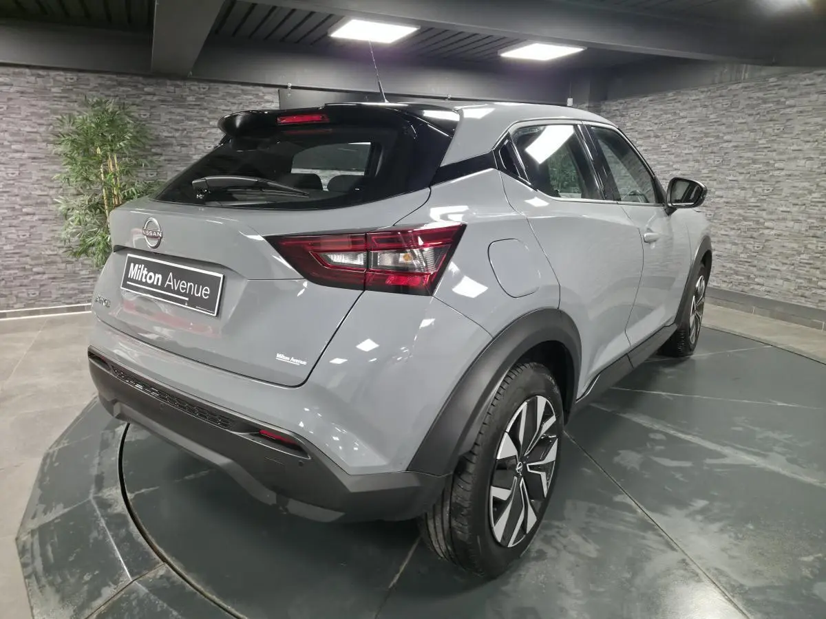 Vue 3/4 arrière droite du Nissan Juke 2023 gris métallisé avec jantes bi-ton et toit noir en intérieur showroom.