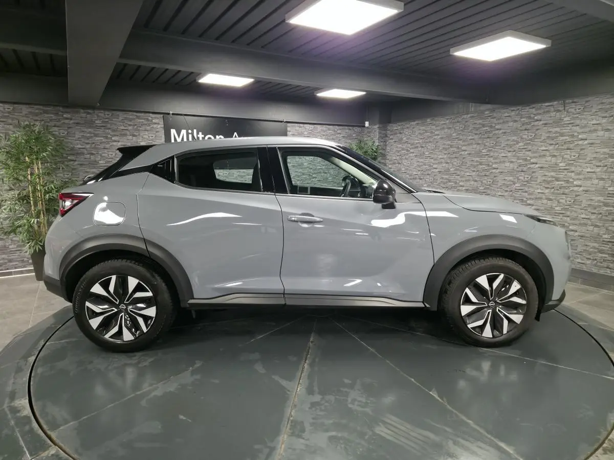 Profil droit d'un Nissan Juke gris métallisé 2023 avec jantes alliage bicolores et coques de rétroviseurs noires.