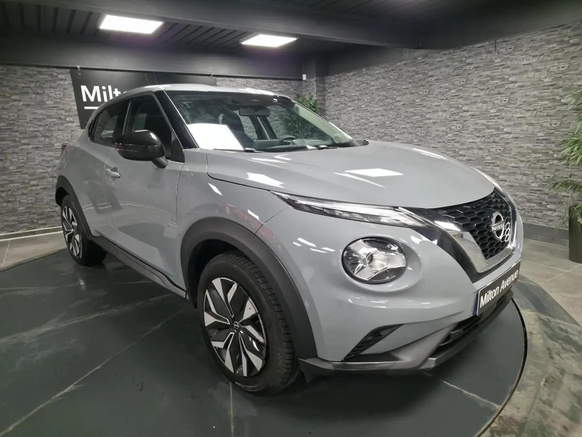 Nissan Juke gris métallisé vue 3/4 avant droit, avec jantes bi-ton et coques de rétroviseurs noires.