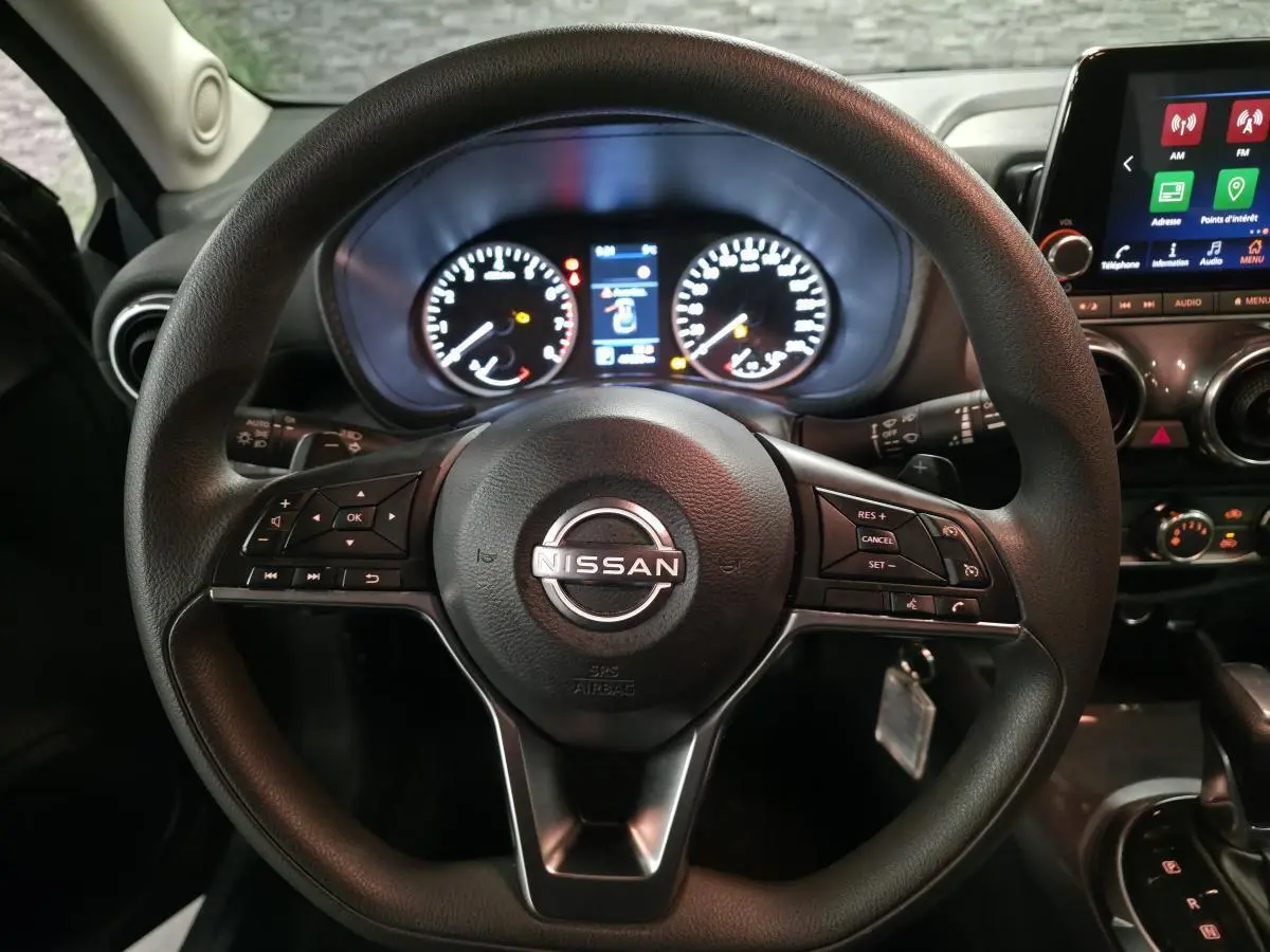 Vue rapprochée du volant noir de Nissan Juke 2023 avec tableau de bord et écran tactile en arrière-plan.