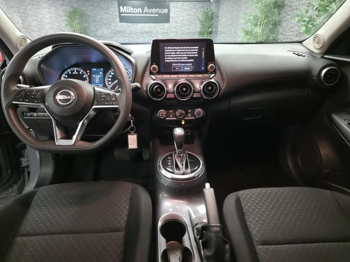 Vue intérieure avant du Nissan Juke gris 2023, tableau de bord avec écran tactile et volant multifonction.