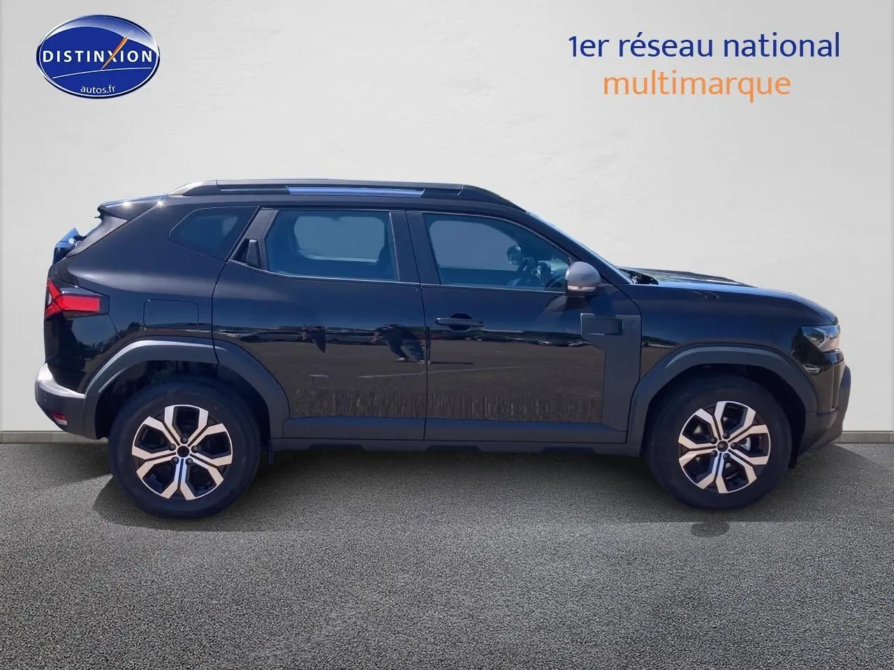 Profil latéral droit du Dacia Duster noir 2025 avec jantes alu et barres de toit visibles sur fond neutre.