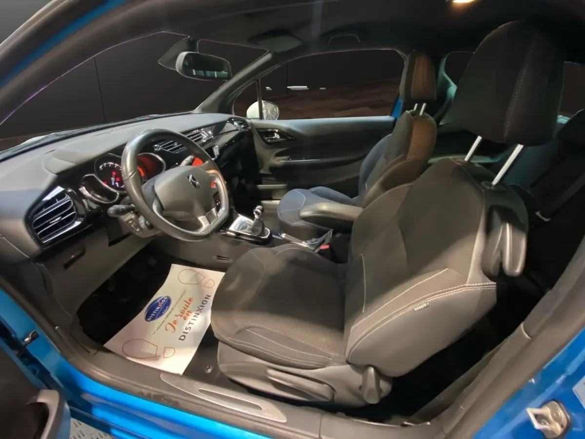 Vue intérieure côté conducteur de la Citroën DS3 e-HDi bleu, volant alu-cuir, sièges noirs et boîte manuelle visible.