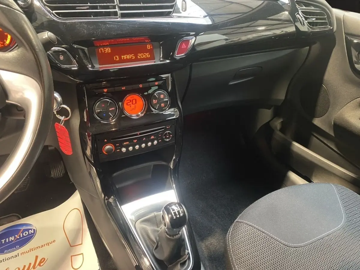Vue intérieure centrée sur la console centrale et levier de vitesses manuelle d'une Citroën DS3 bleu, avec tableau de bord noir brillant.