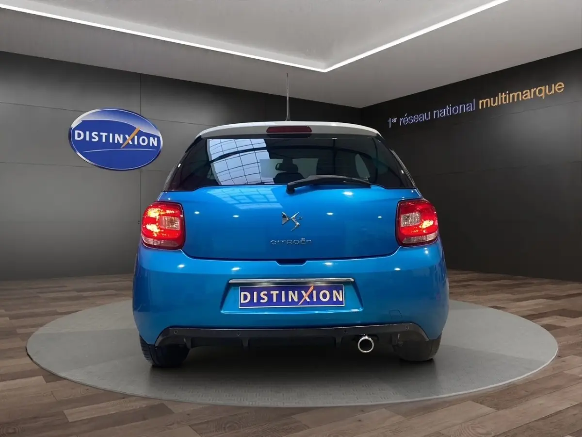 Vue arrière d'une Citroën DS3 e-HDi 90 Airdream So Chic bleu avec feu arrière allumé dans un showroom.