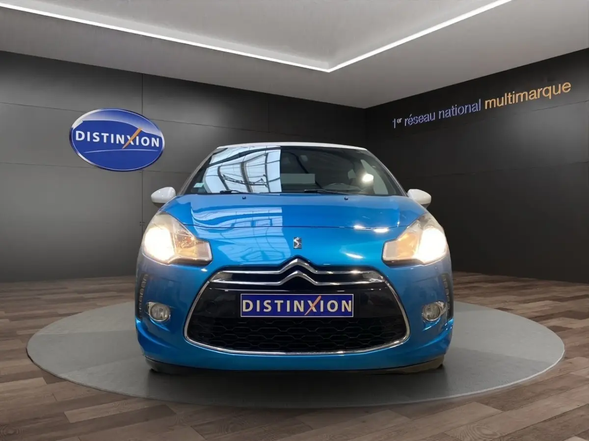 Vue avant d'une Citroën DS3 e-HDi 90 Airdream So Chic bleu avec phares allumés en showroom.
