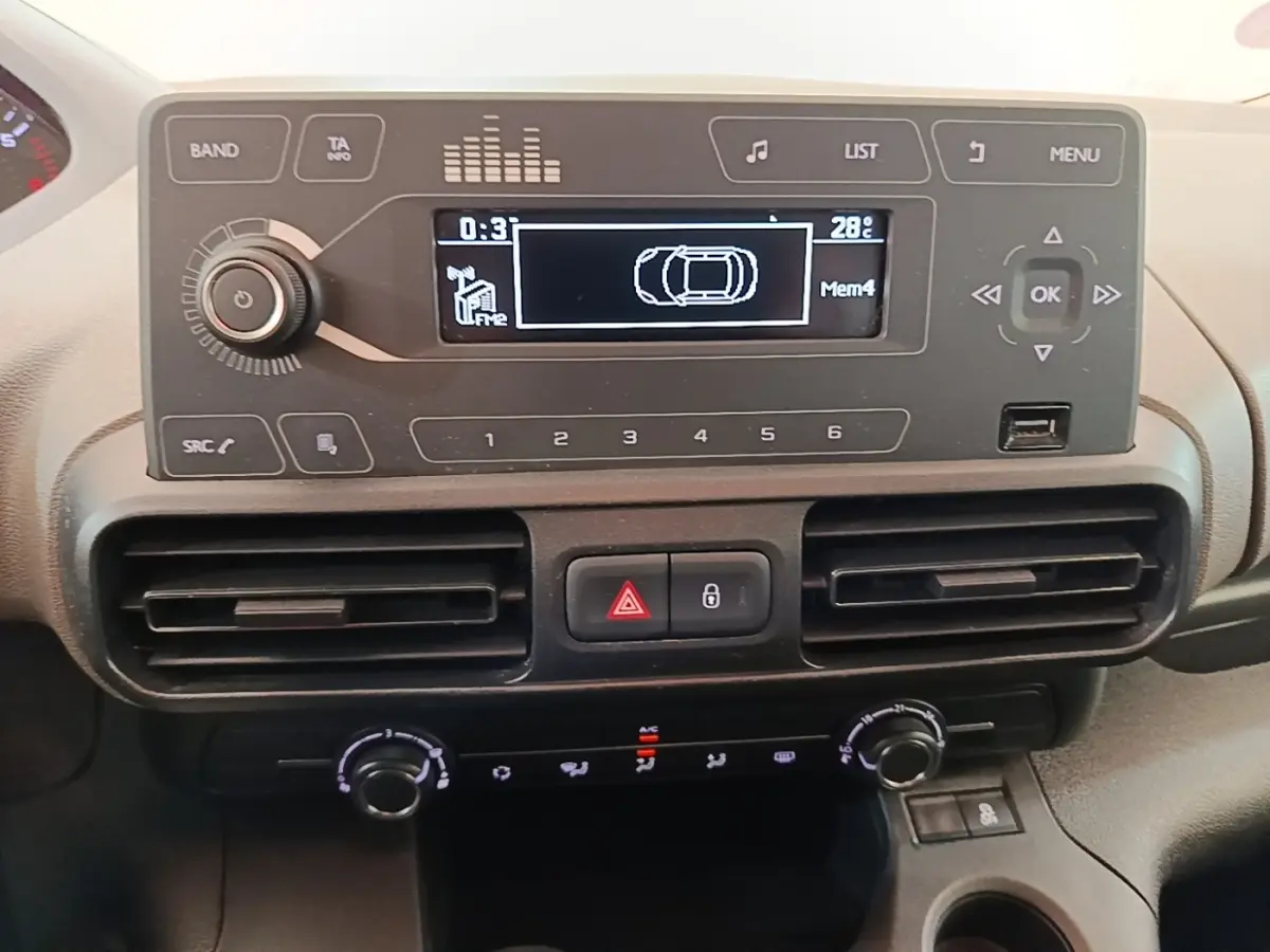 Vue rapprochée du tableau de bord du Peugeot Rifter avec écran multifonction et commandes de climatisation noires.