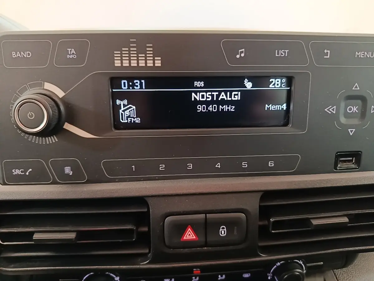 Vue rapprochée du tableau de bord du Peugeot Rifter blanc, affichant l'autoradio avec station Nostalgie à 90,40 MHz.