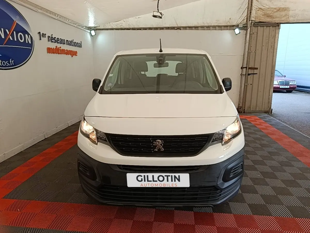 Vue avant d'un Peugeot Rifter blanc 2020 avec calandre noire et phares allumés dans un garage.