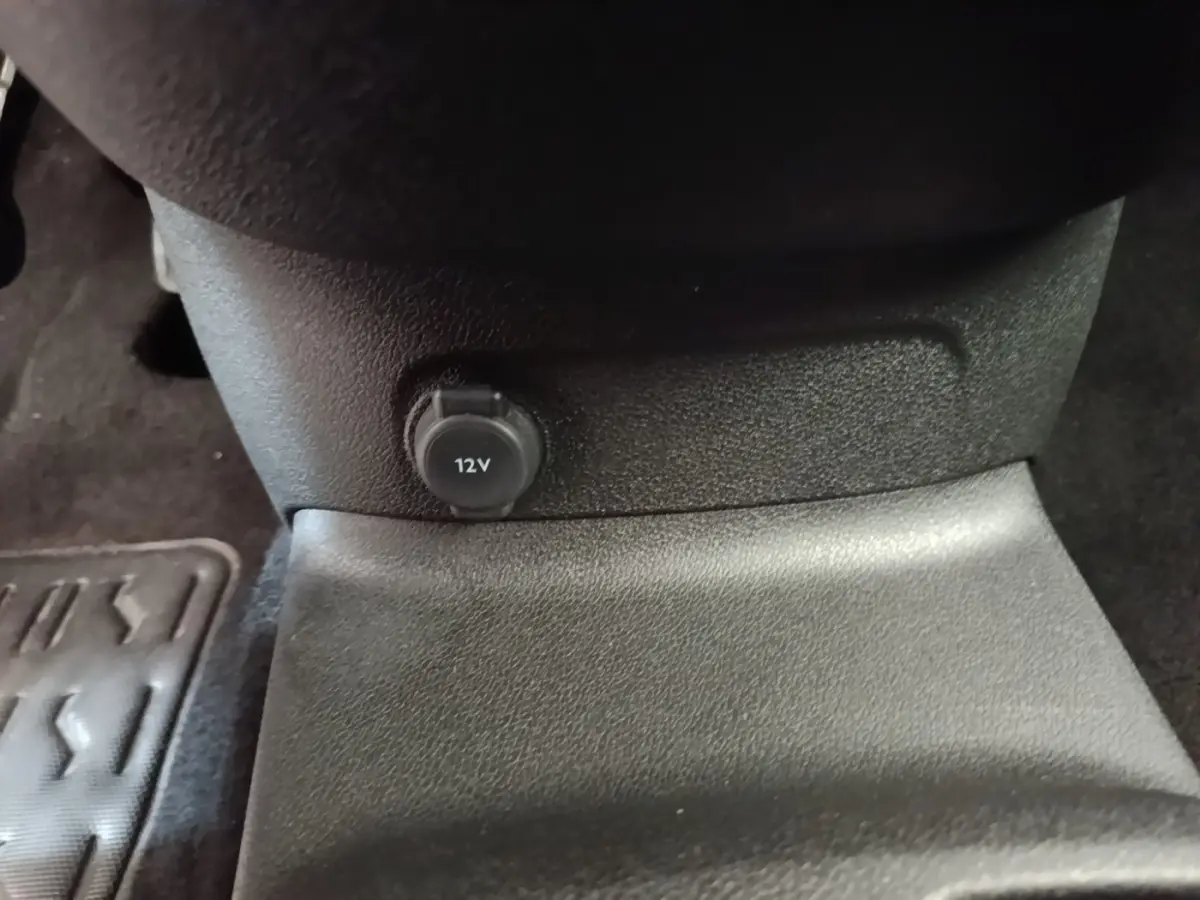 Prise 12V noire en gros plan sur la console centrale intérieure du Peugeot Rifter blanc, vue rapprochée du bas.