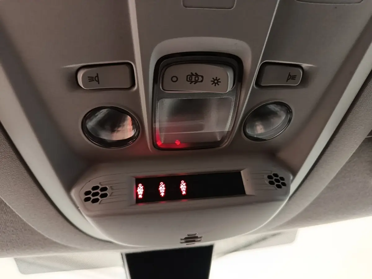 Vue en gros plan du plafonnier intérieur du Peugeot Rifter blanc, avec commandes d’éclairage et voyants de ceinture allumés.