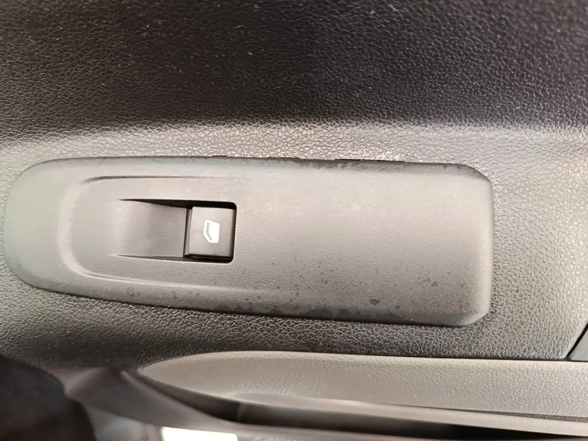 Gros plan sur l'interrupteur de lève-vitre électrique noir sur la porte intérieure d'un Peugeot Rifter blanc.