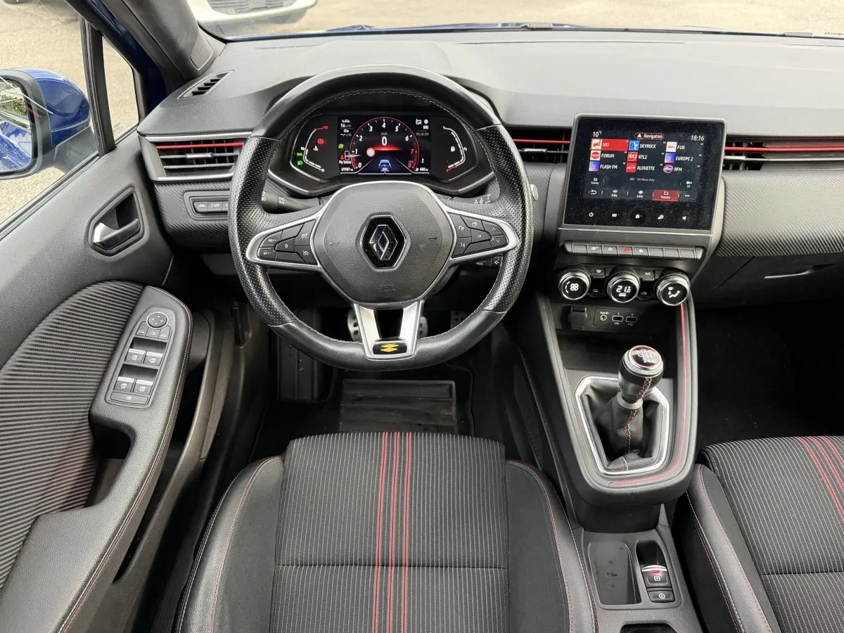 Vue intérieure avant de la Renault Clio RS Line TCe 140 2021, volant cuir, écran tactile et sièges noirs à surpiqûres rouges.