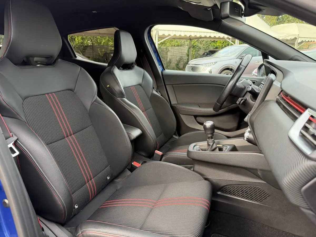 Vue intérieure côté conducteur de la Renault Clio RS Line bleu 2021, sièges sport noirs avec surpiqûres rouges.