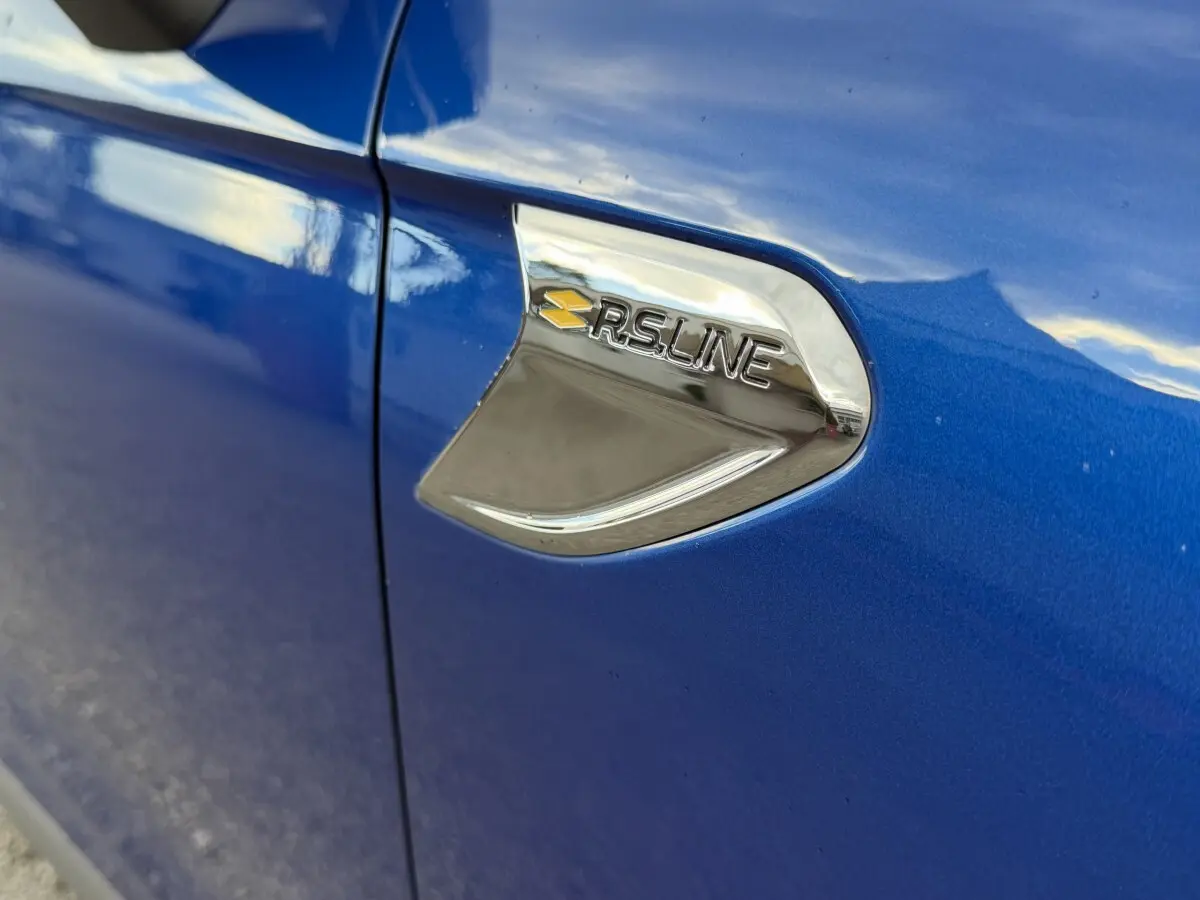 Gros plan sur l'emblème RS Line chromé sur la portière côté gauche d'une Renault Clio bleue.