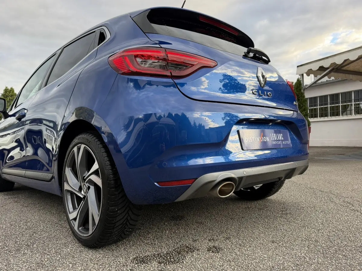 Vue 3/4 arrière droite d'une Renault Clio RS Line bleu, avec échappement chromé et jantes alliage distinctives.