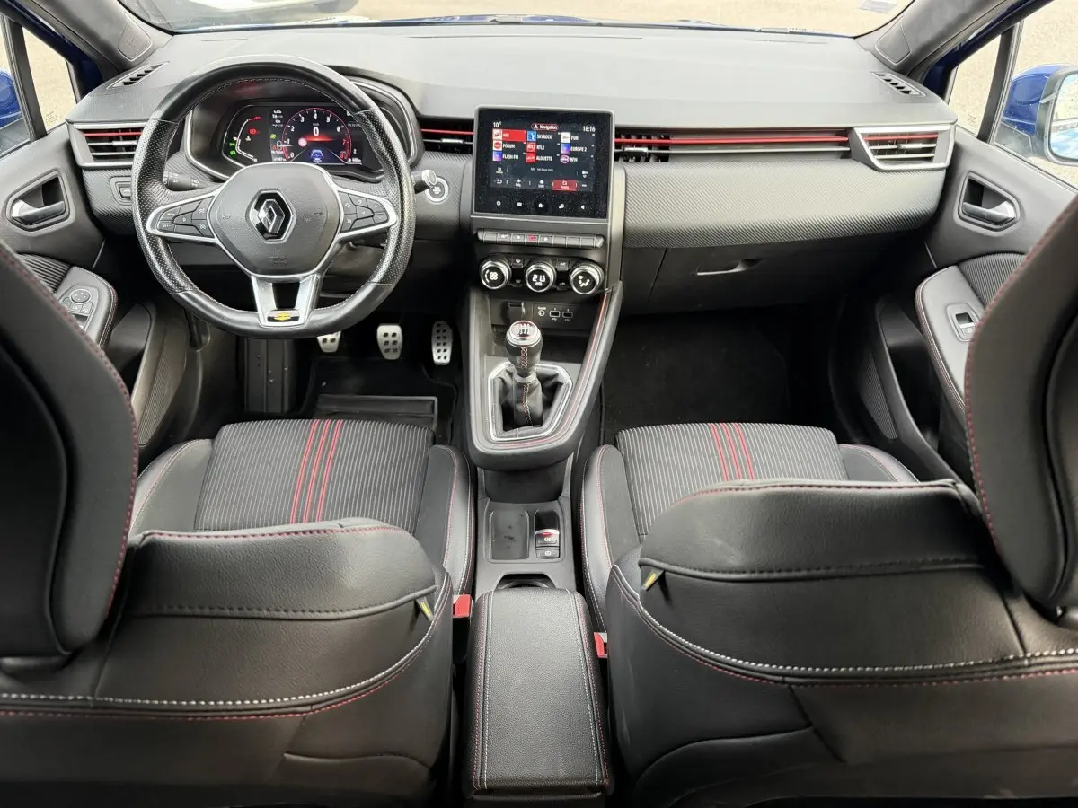 Vue intérieure avant de la Renault Clio RS Line 2021, sièges noirs avec surpiqûres rouges et volant cuir multifonction.