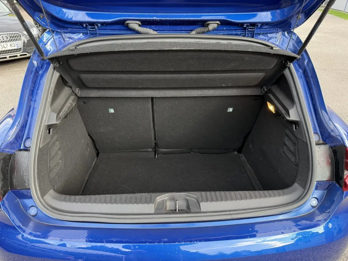 Coffre ouvert vu de l'arrière d'une Renault Clio RS Line bleu, montrant l'espace de chargement et la lumière intérieure.