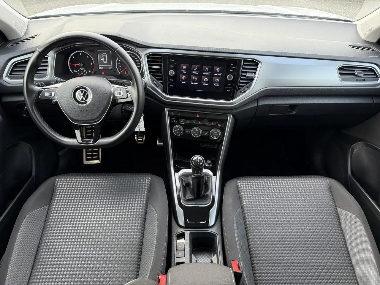 Vue intérieure du tableau de bord et console centrale du Volkswagen T-Roc 2.0 TDI avec volant cuir et levier de vitesses manuel.