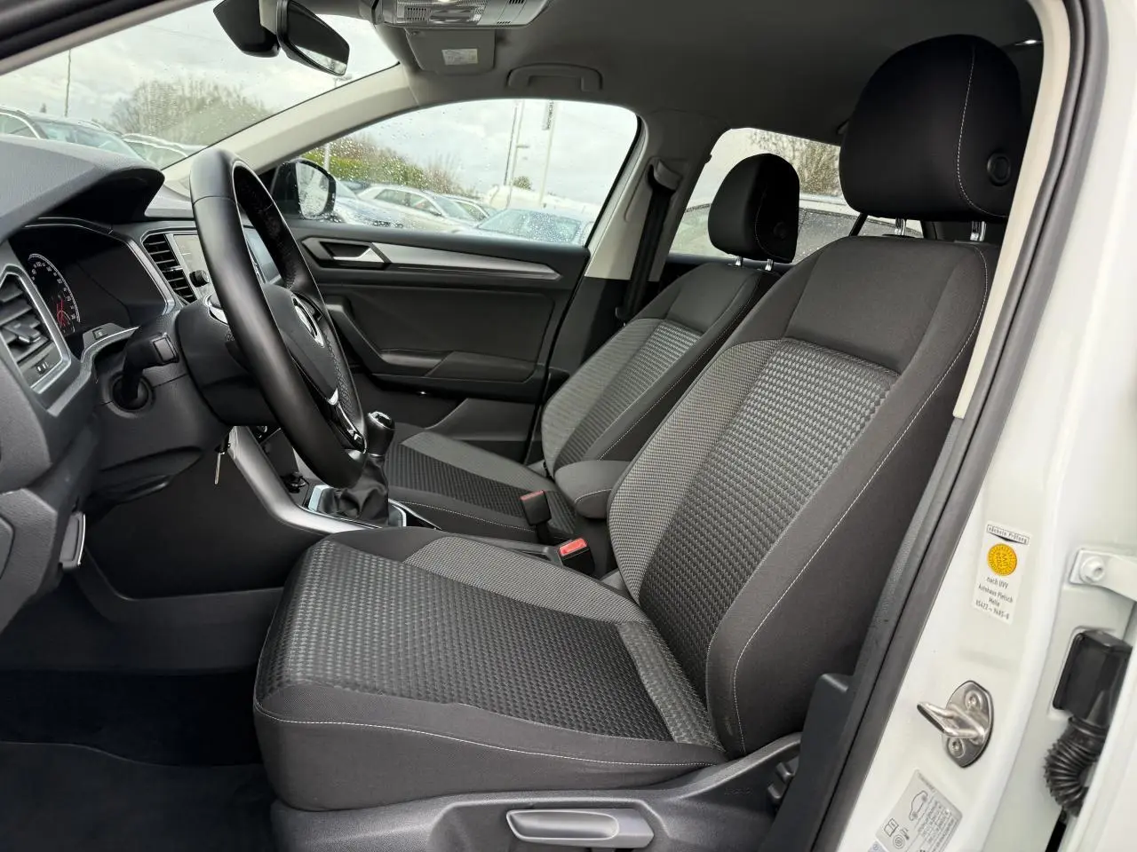 Vue intérieure côté conducteur du Volkswagen T-Roc blanc pur 2021, sièges avant en tissu gris et volant cuir multifonction.