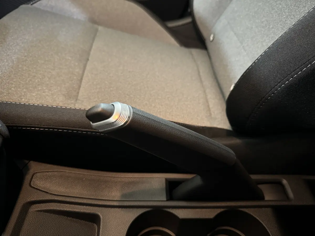 Gros plan sur le frein à main manuel noir et gris, avec siège tissu gris clair de la Renault Clio Evolution Blue dCi 2025.