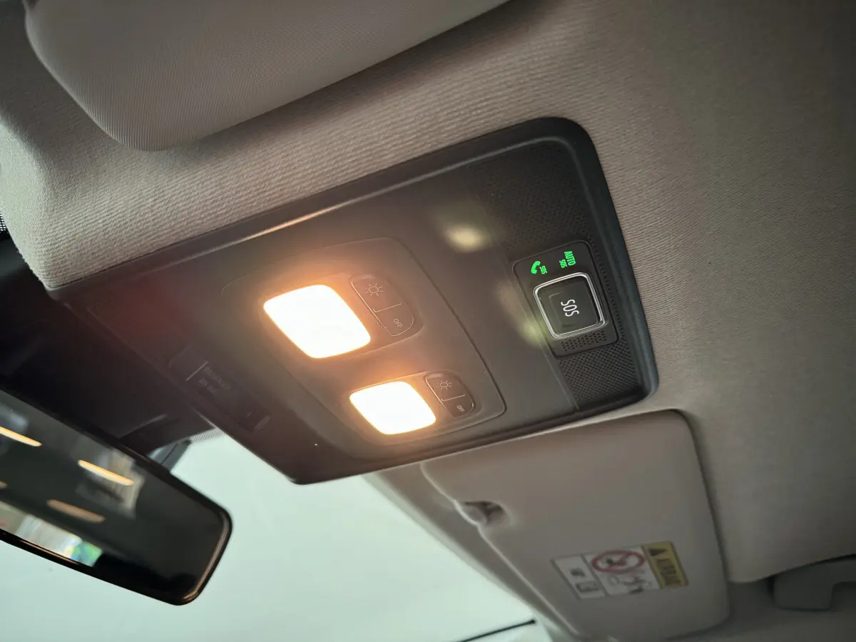 Plafonnier intérieur allumé avec bouton SOS vert sur Renault Clio gris clair, vue en contre-plongée depuis l'avant.