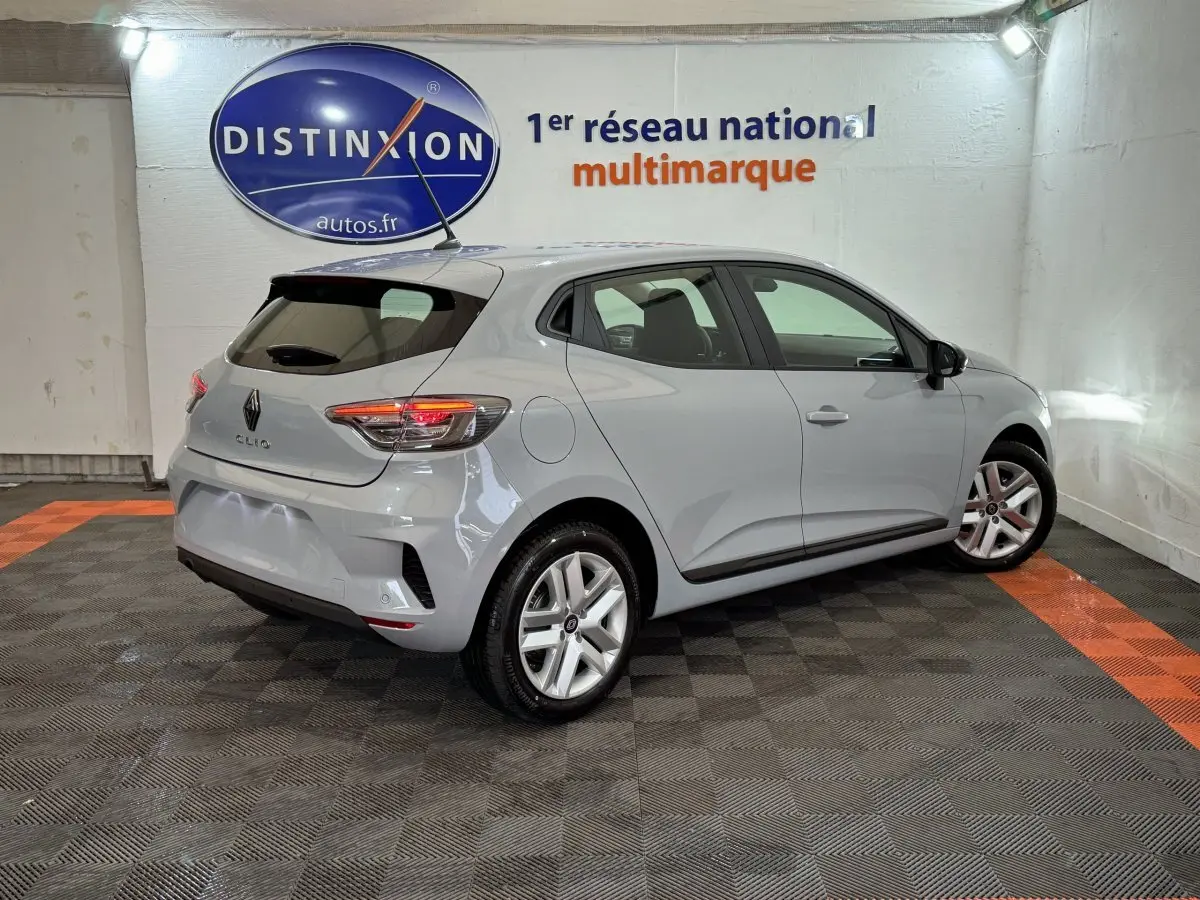 Vue 3/4 arrière droite d'une Renault Clio gris clair Evolution Blue dCi 100 en intérieur, avec feux arrière allumés.