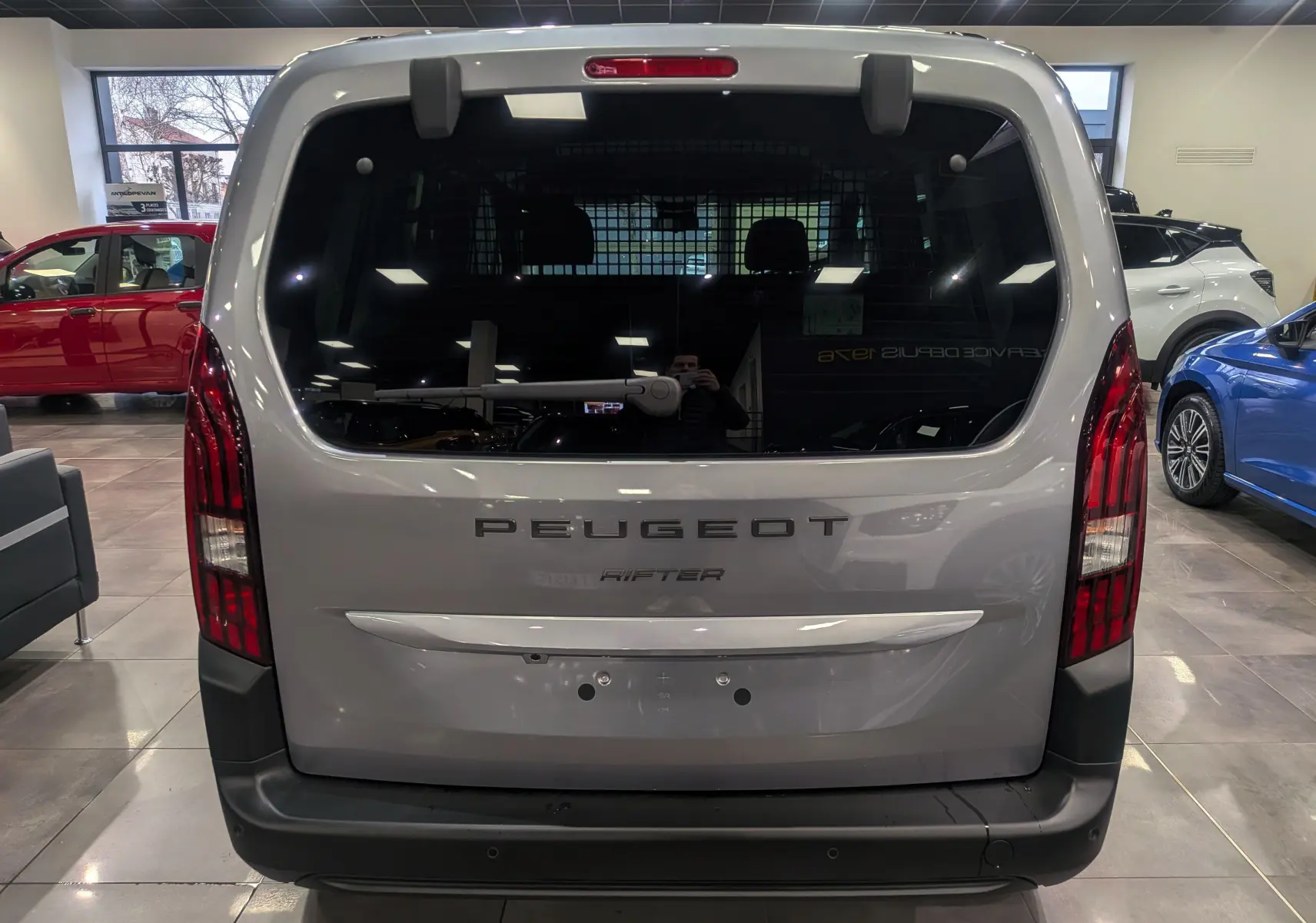 Vue arrière d'un Peugeot Rifter gris acier 2025 avec hayon vitré et feux arrière verticaux en concession.