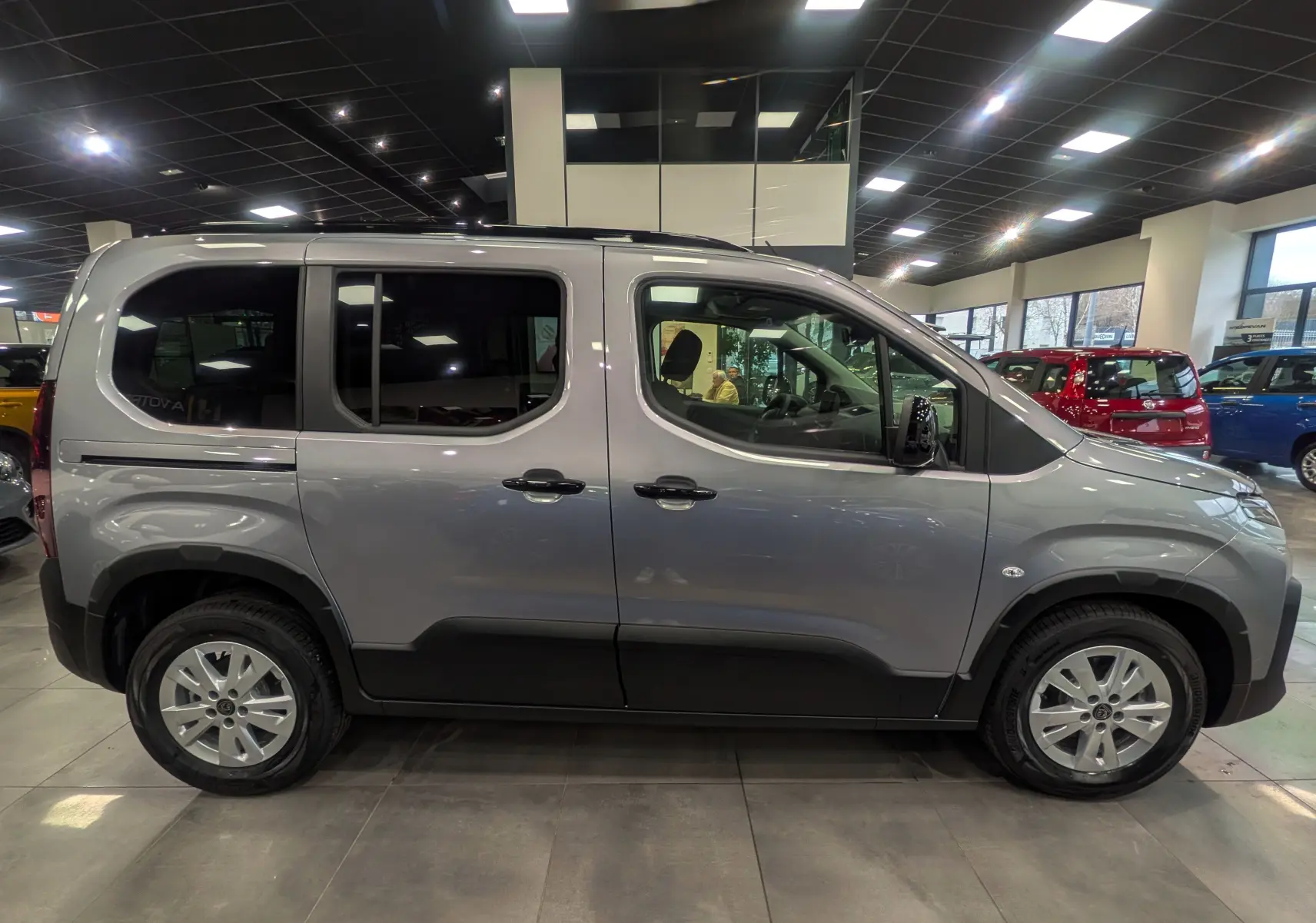 Vue de profil côté gauche d'un Peugeot Rifter gris acier 2025 en version M BlueHDi 130 S&S EAT8 5 places, avec jantes alliage et protections noires.