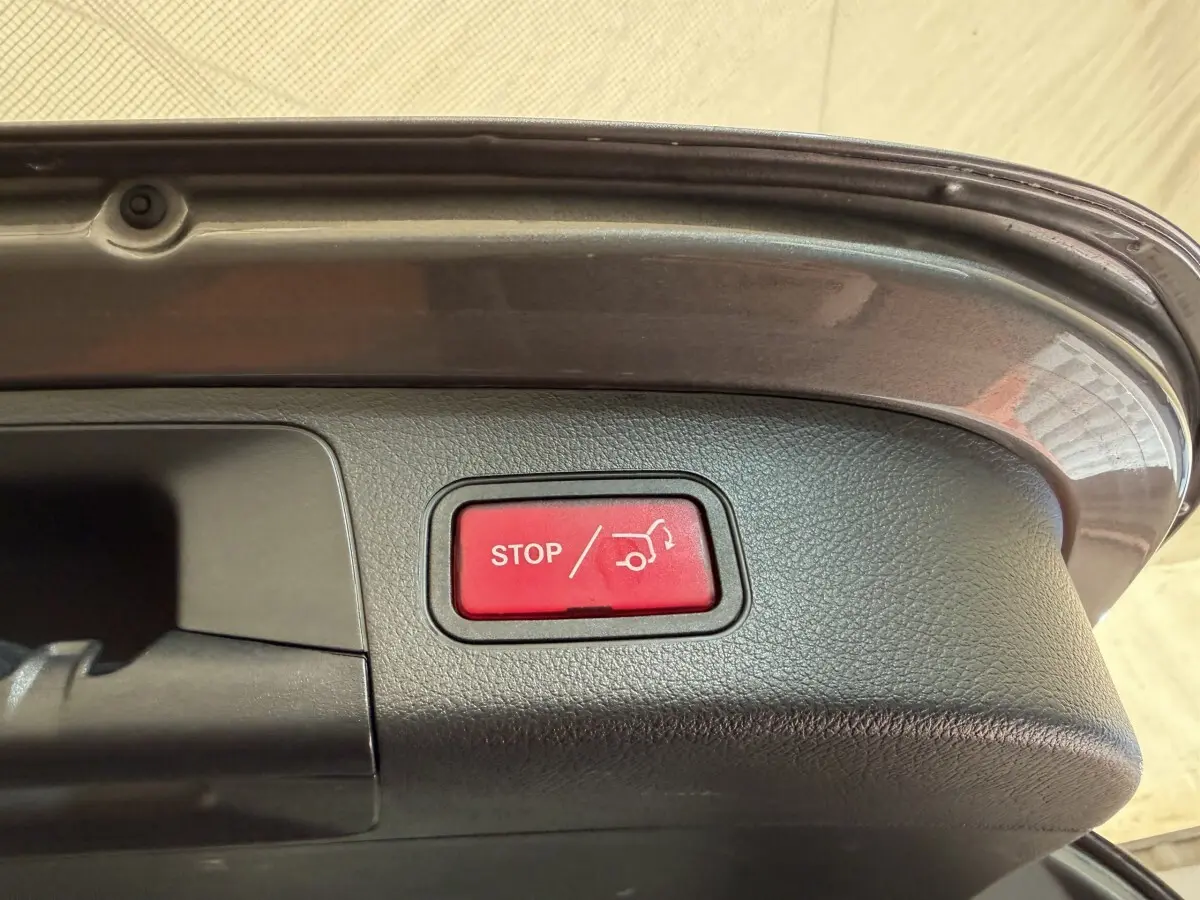 Bouton rouge stop ouverture coffre visible sur le bord intérieur du hayon gris clair d’un Mercedes GLA 250 e AMG Line 2023.
