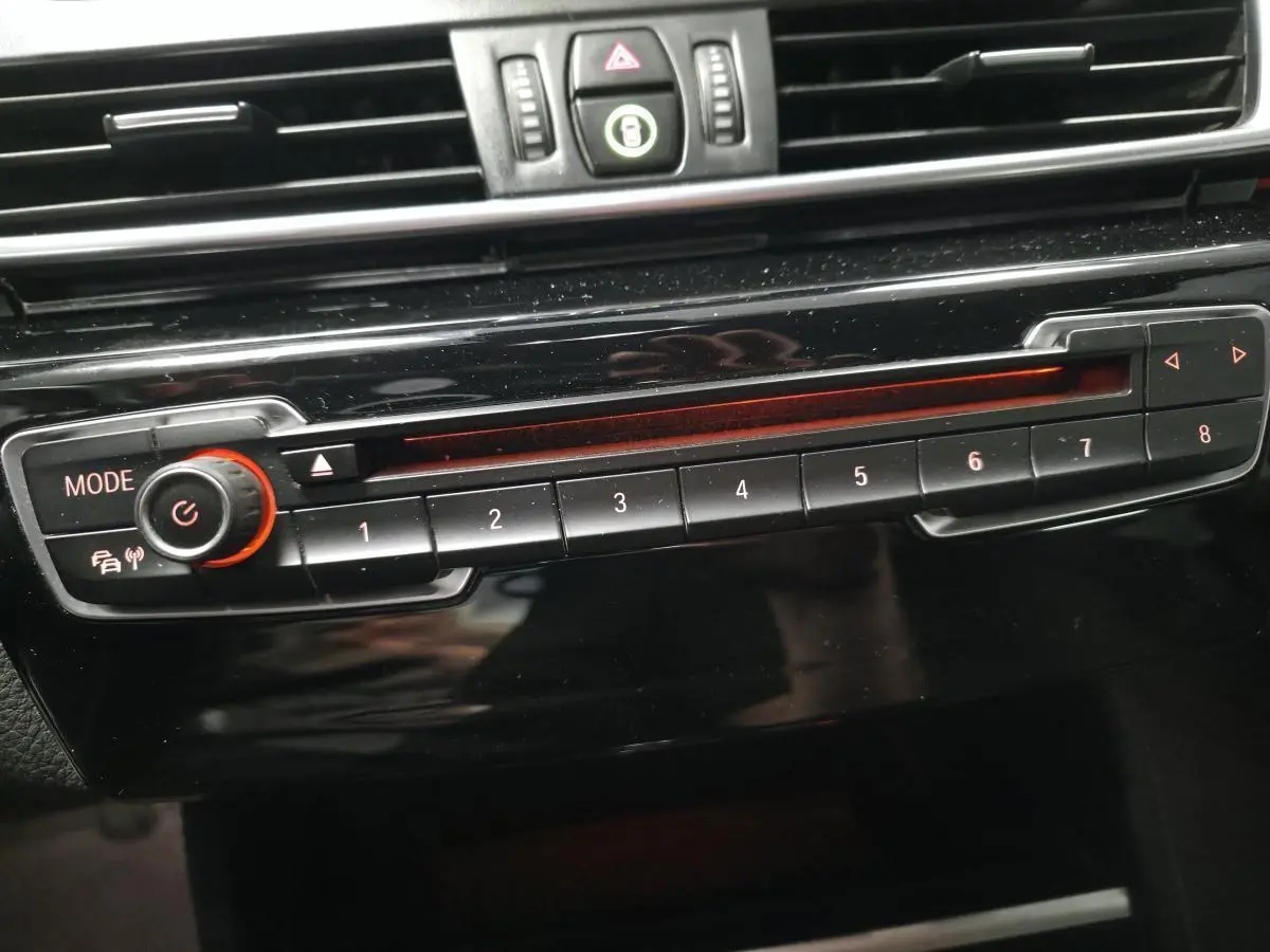 Gros plan sur la commande radio BMW noire avec boutons numérotés et éclairage rouge à l'intérieur du véhicule.