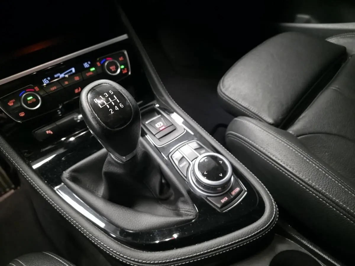 Gros plan sur la console centrale intérieure noire d'une BMW Série 2 218d xDrive avec levier de vitesse manuel et commandes iDrive.