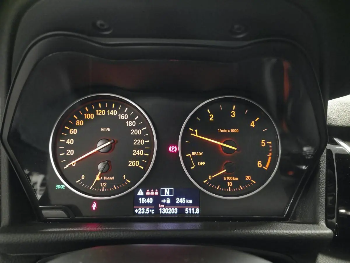 Vue rapprochée du tableau de bord noir d'une BMW Série 2 218d xDrive avec compteurs analogiques orange et écran digital central.