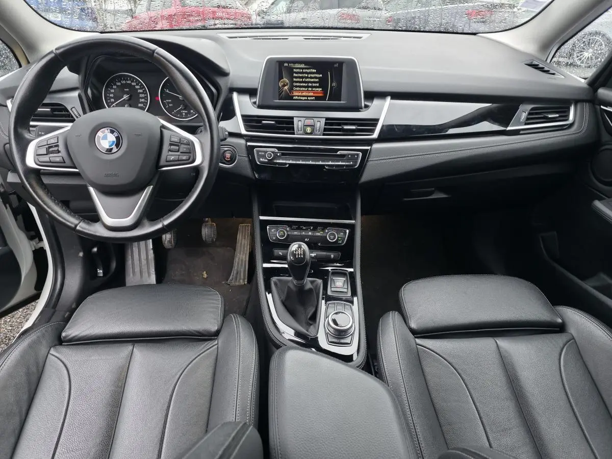 Vue intérieure avant de la BMW Série 2 Gran Tourer 218d xDrive 2016, volant cuir, console centrale avec boîte manuelle.