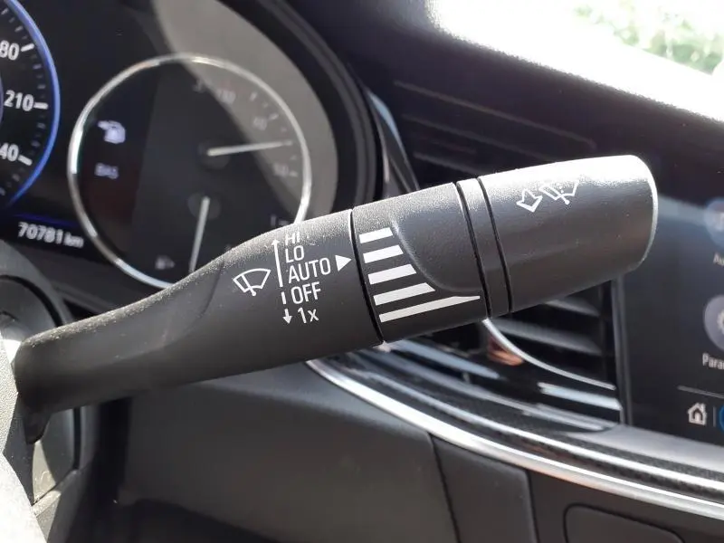 Gros plan sur le commodo de l’essuie-glace dans l’habitacle de l’Opel Insignia Grand Sport gris clair, tableau de bord en arrière-plan.
