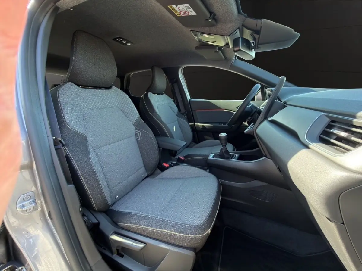 Vue intérieure côté conducteur de la Renault Captur gris foncé 2024, sièges tissu et volant multifonctions.