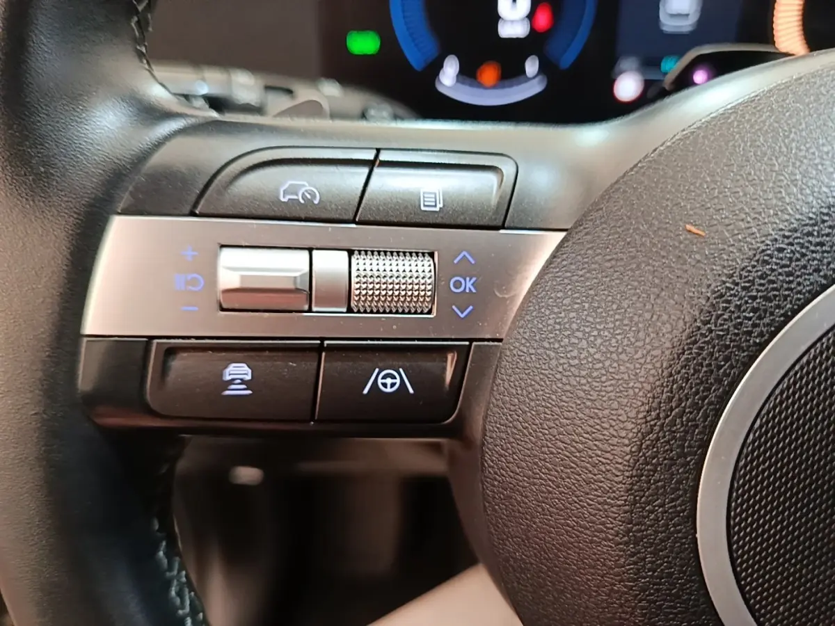 Gros plan sur les commandes gauche du volant cuir du Hyundai Kona 1.6 Hybrid 2024, avec touches d’aide à la conduite.